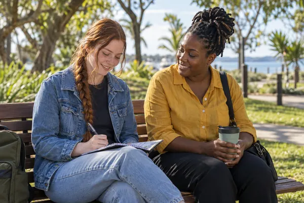 Support worker and young adult sitting side by side on a quiet park bench