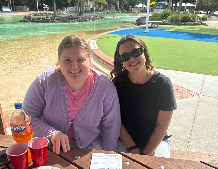 Two women smiling together at a picnic table by a lagoon on a community outing